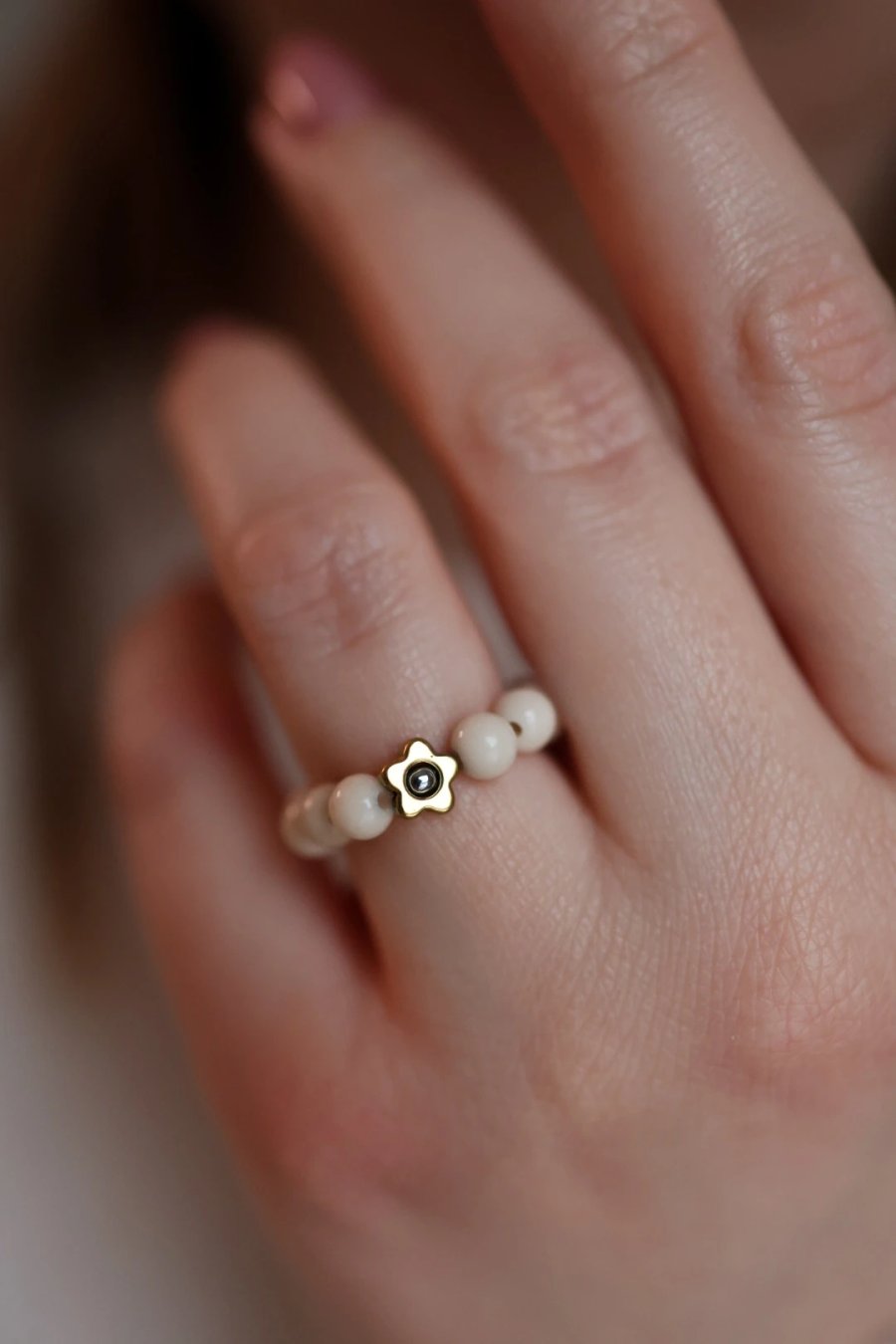 Elastische ring van crèmekleurige rivierstenen met een bloemetje van tweekleurig hematiet in goud, handmade